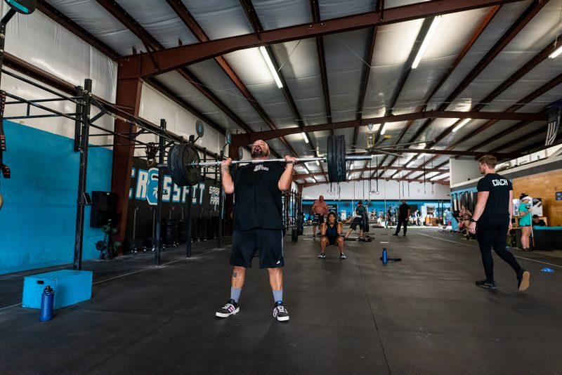 Athlete pressing a loaded barbell overhead while other members finish a conditioning workout